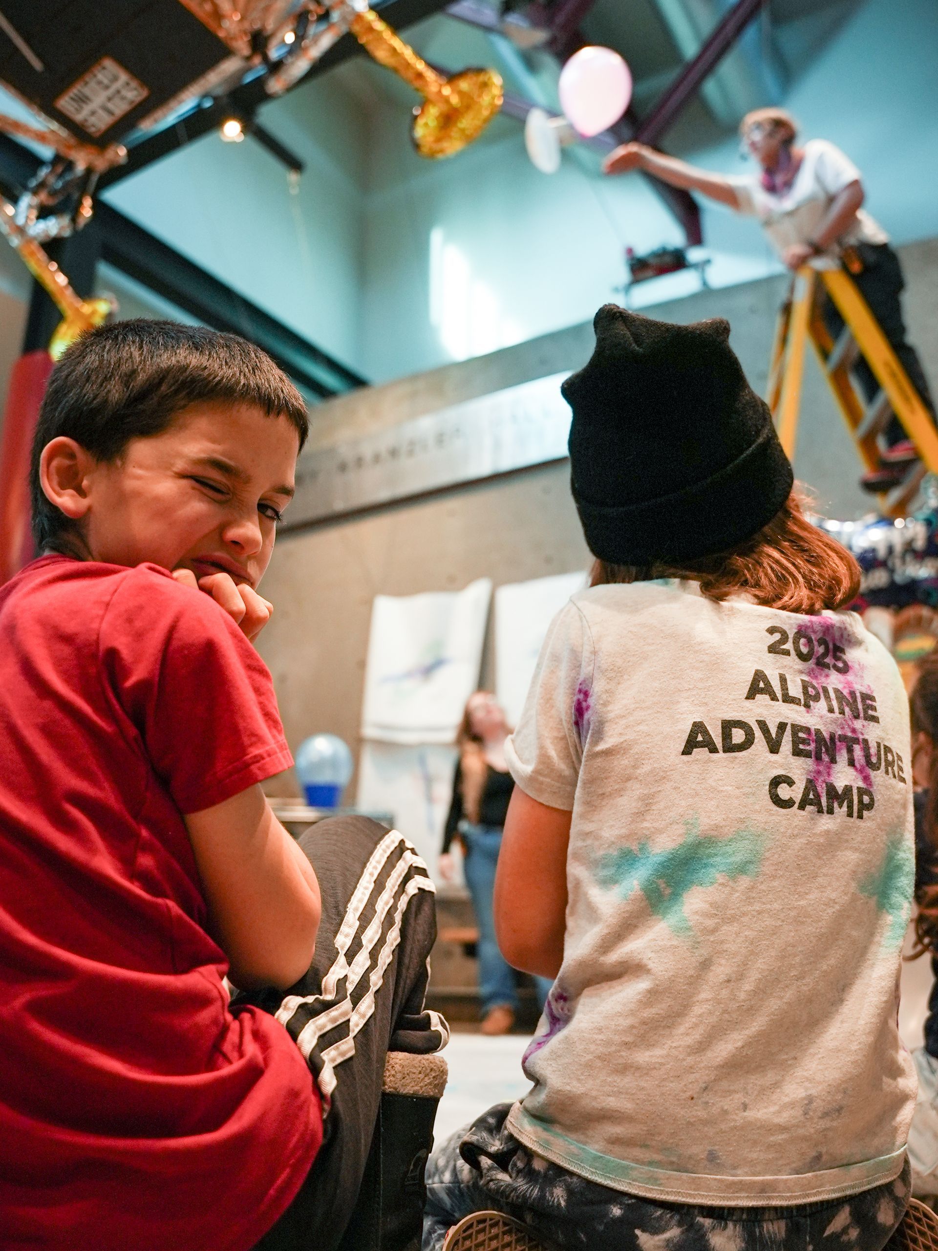 Boy looking at the camera winks near a another child wearing a 