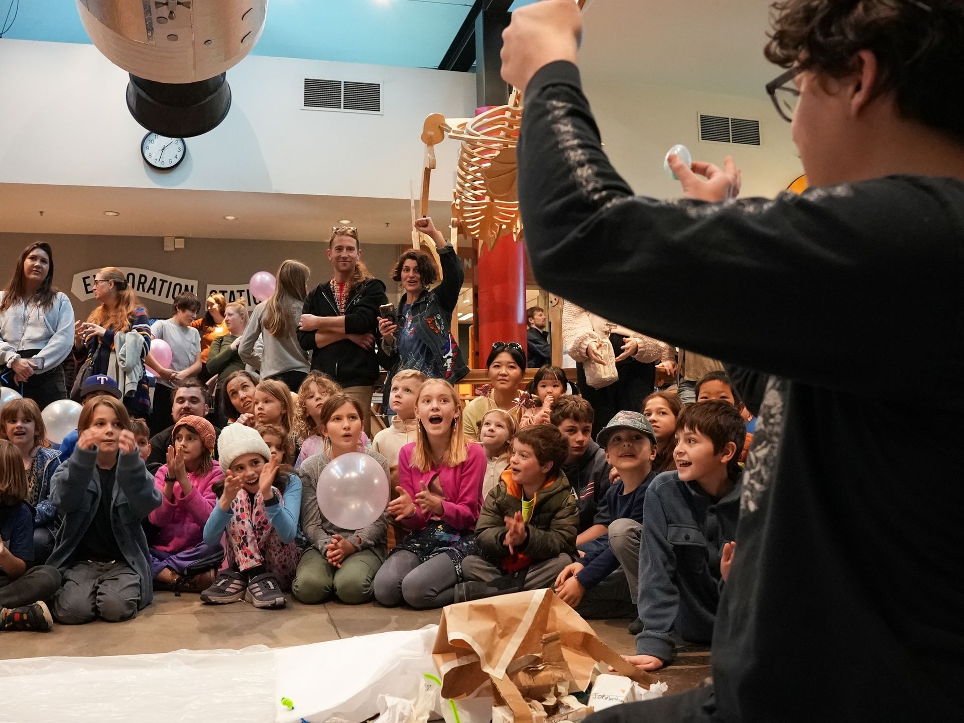 Boy demonstrating a science experiment to a group of children, indoors. Children watch with excitement at ScienceWorks.