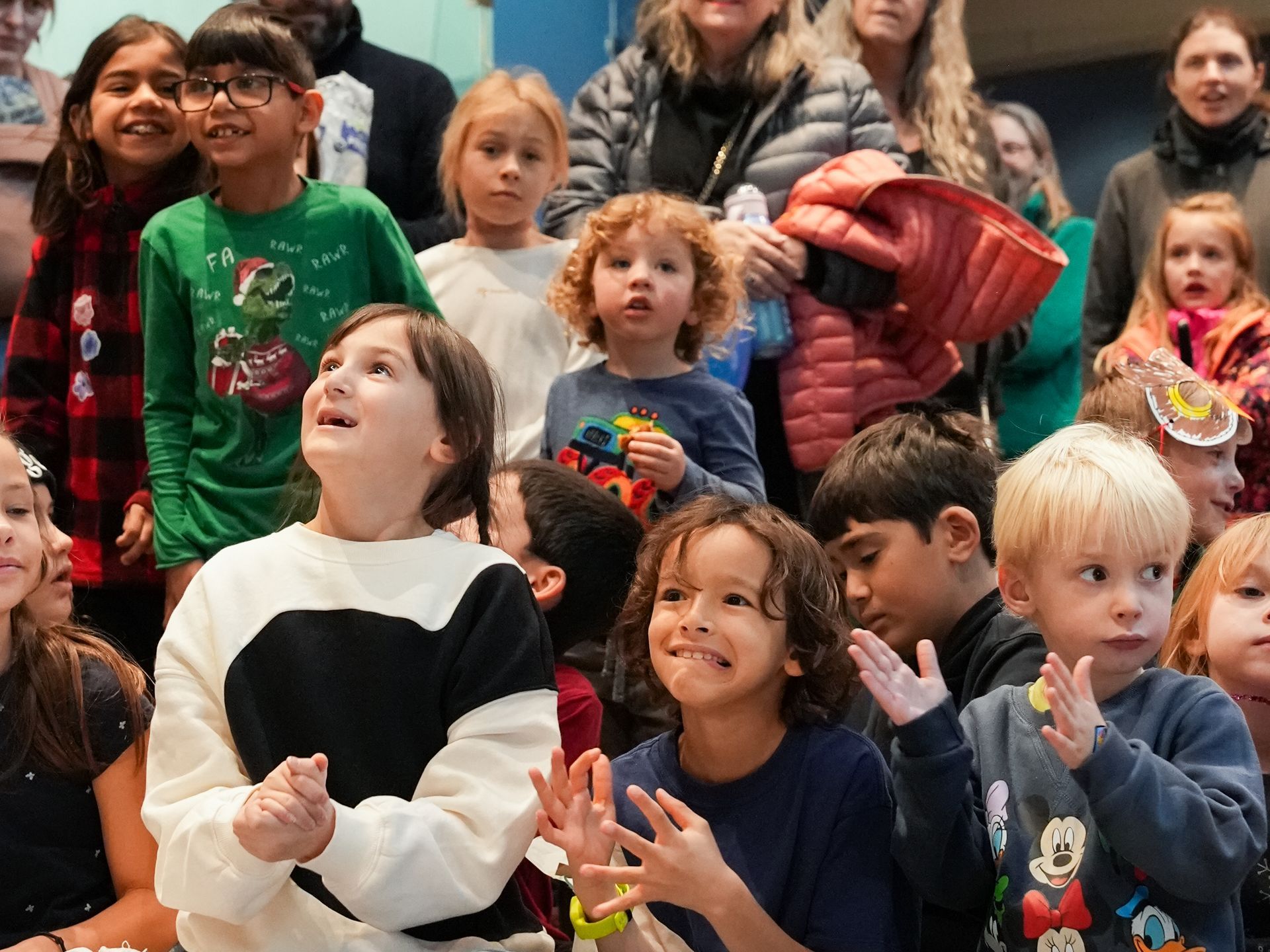 Children looking upwards, smiling, and clapping in a crowded room at ScienceWorks.
