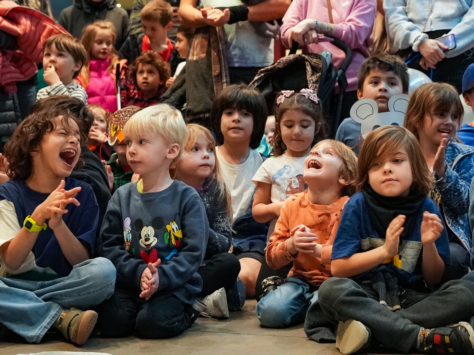 Children seated on floor, some laughing and clapping. Audience in background at ScienceWorks.