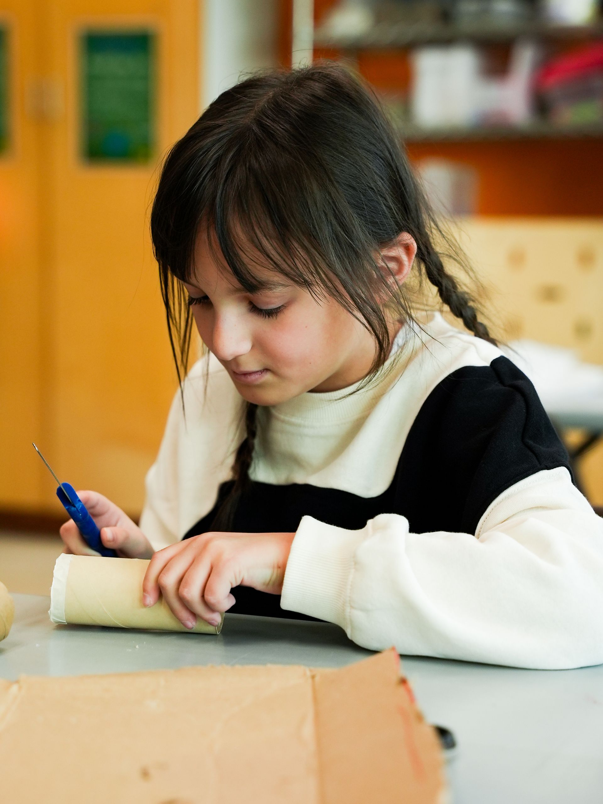 Girl focused on crafting with a tool, working on a cylindrical object indoors at ScienceWorks.