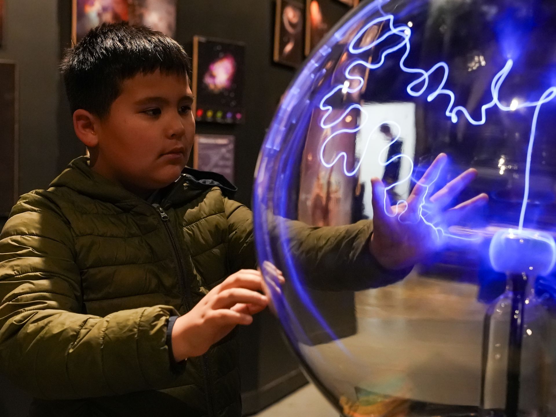 Boy touches plasma globe, causing bright blue lightning bolts to arc from it at ScienceWorks.