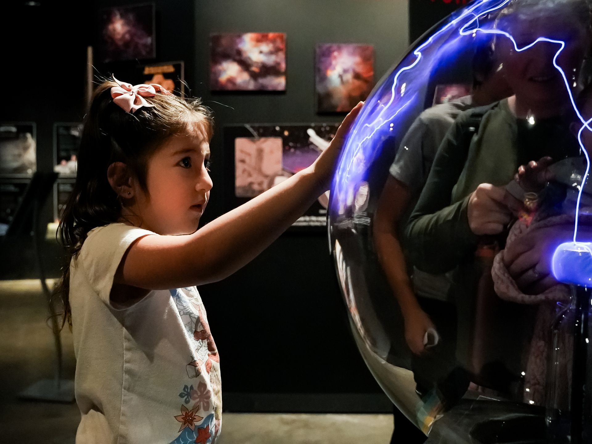 Girl touches a plasma ball, blue arcs of electricity visible at ScienceWorks.