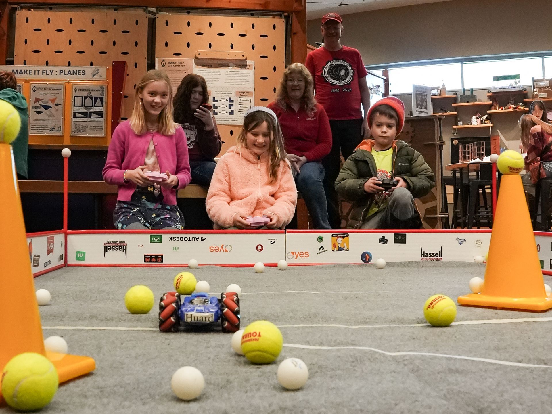 Children operating robots  at ScienceWorks, surrounded by tennis balls and spectators.