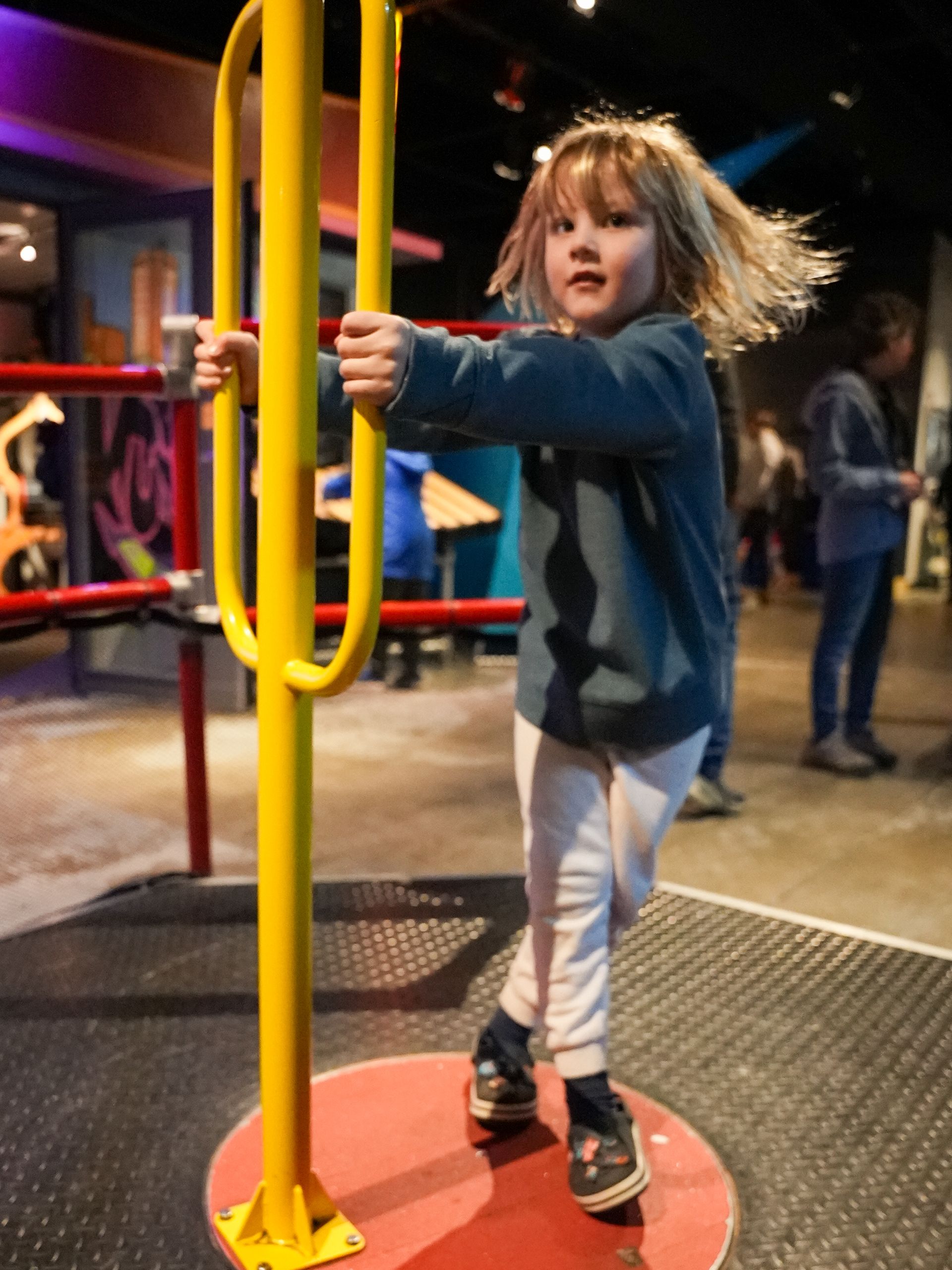 Child spinning on a yellow playground apparatus, hair flying, indoors at ScienceWorks.