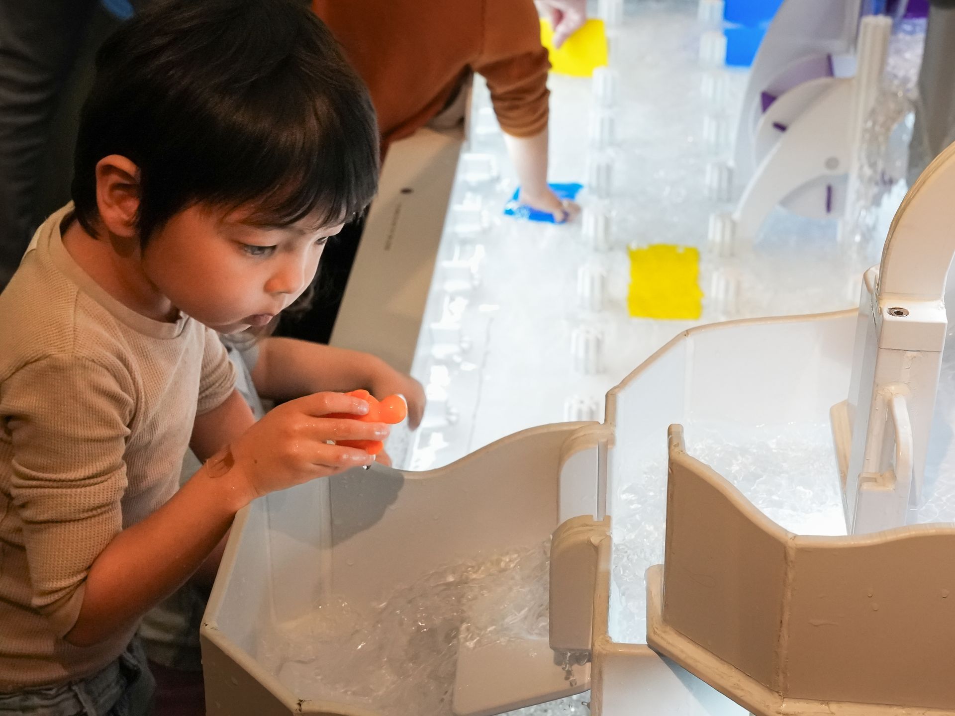 Boy playing with a toy in a water table. He watches as a toy floats at ScienceWorks