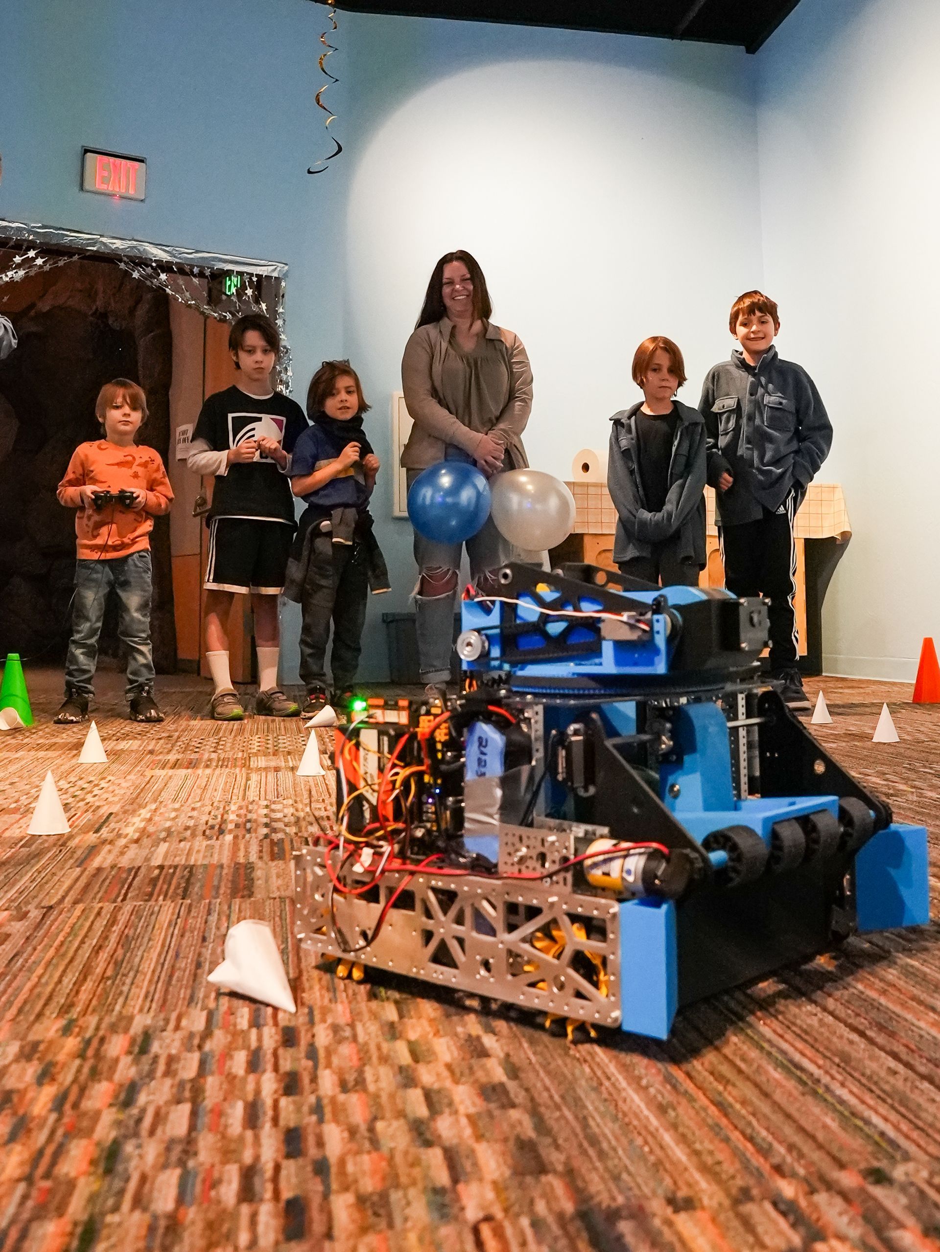 Blue robot with a team of kids and an adult, indoors at ScienceWorks.