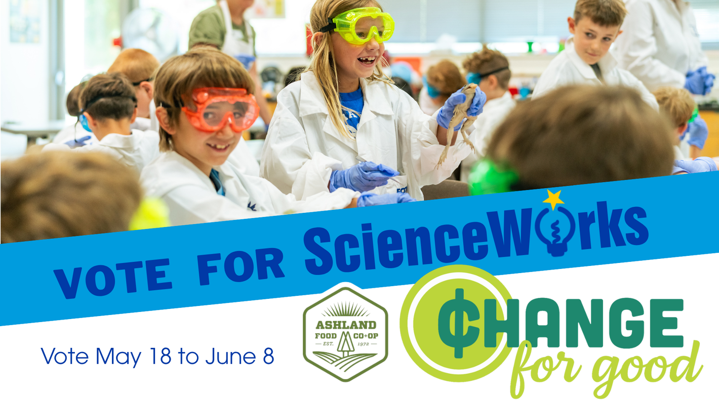 Students in lab coats and goggles promote “Vote for ScienceWorks” and “Change for Good” banners