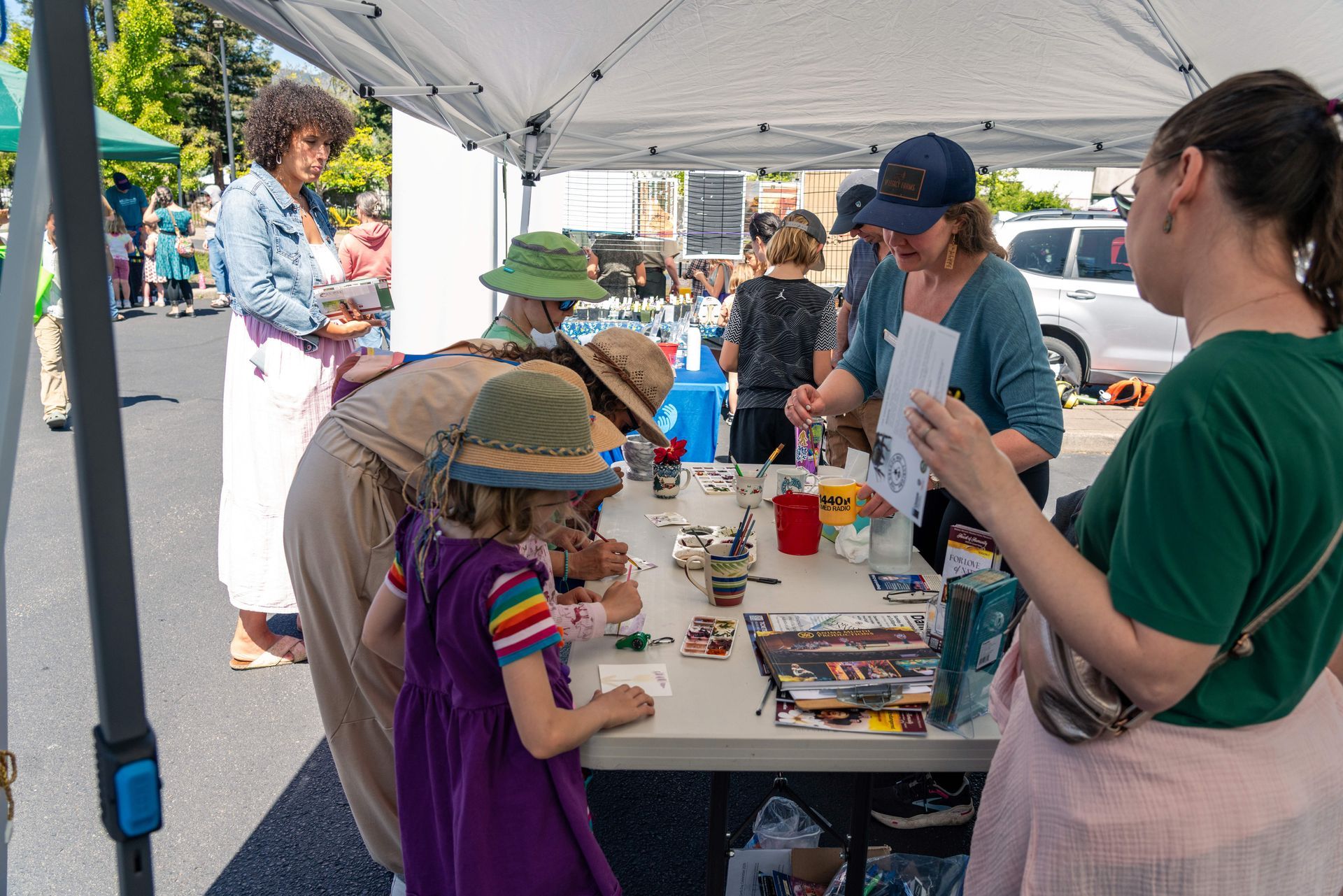 People at a community outreach booth under a white tent, with children gathered around tables of materials.