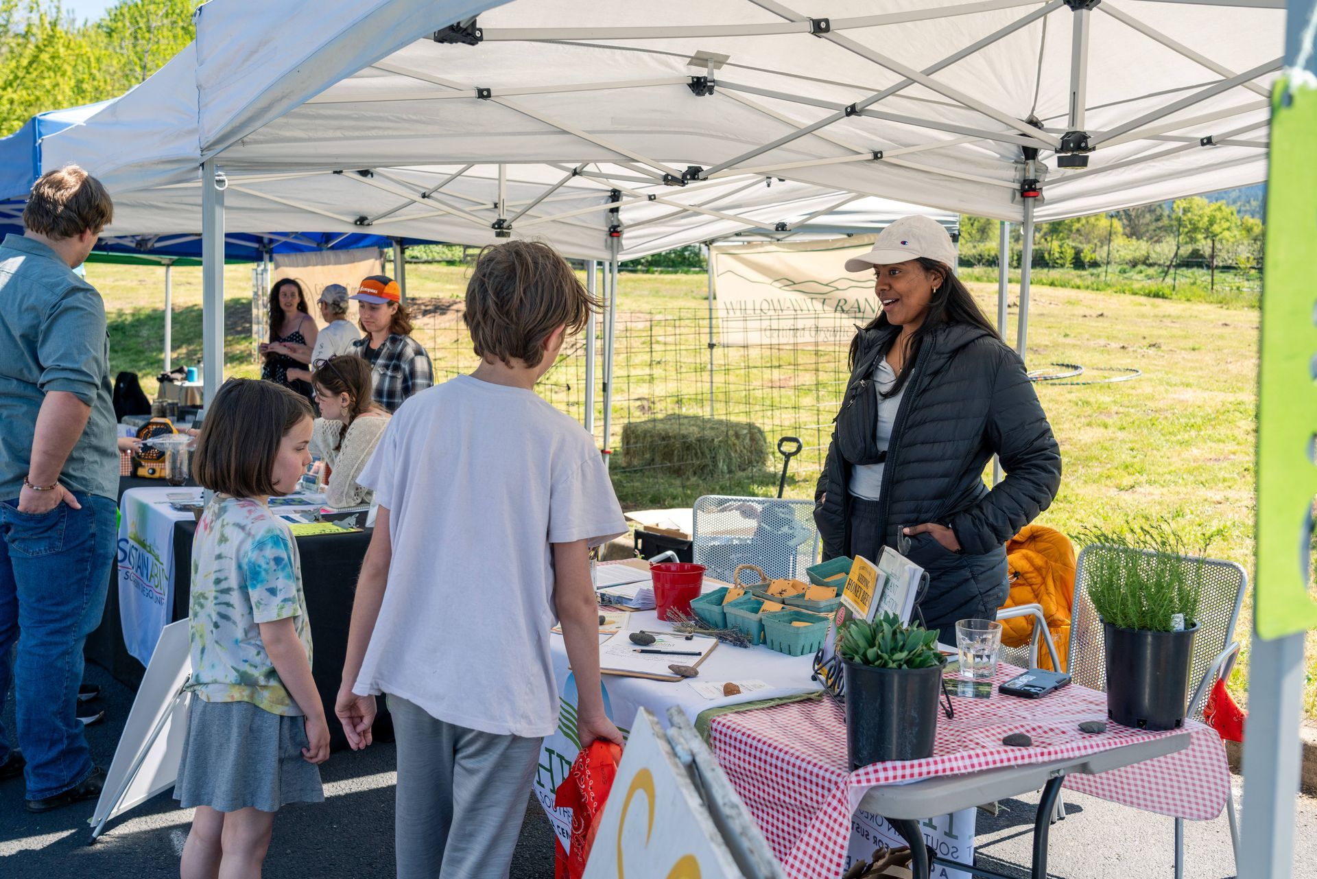 People at a community outreach booth under a white tent, with children gathered around tables of materials.