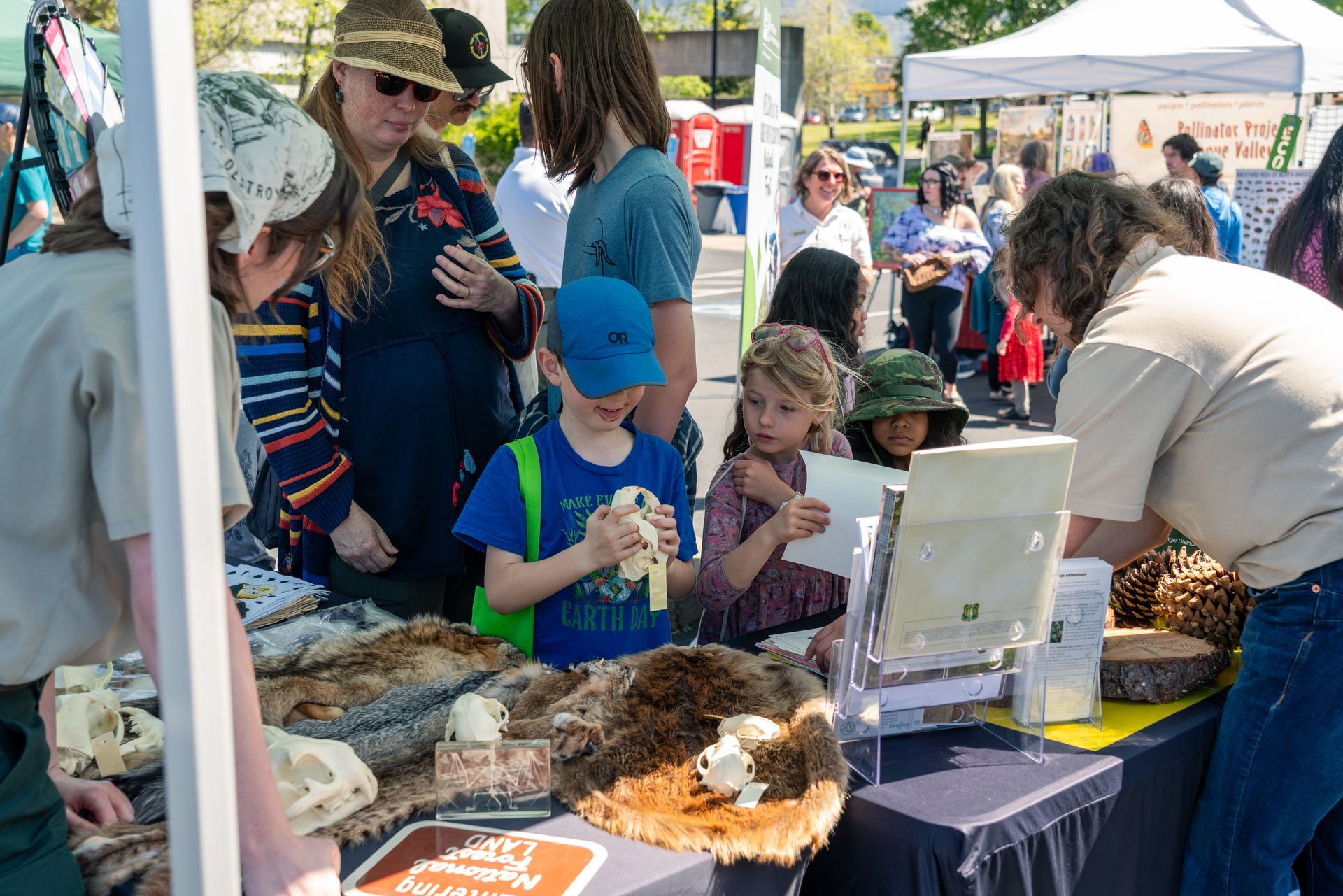 People at a community outreach booth under a white tent, with children gathered around tables of materials.