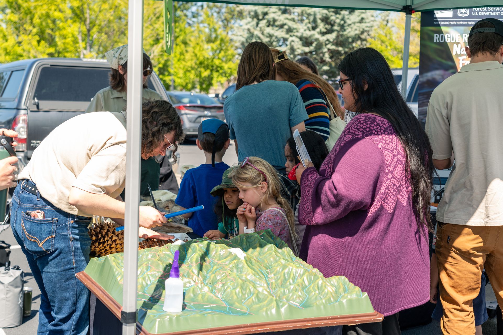People gathered around a table under a canopy looking at a 3D model of the cascade range at the earth day celebration at scienceworks