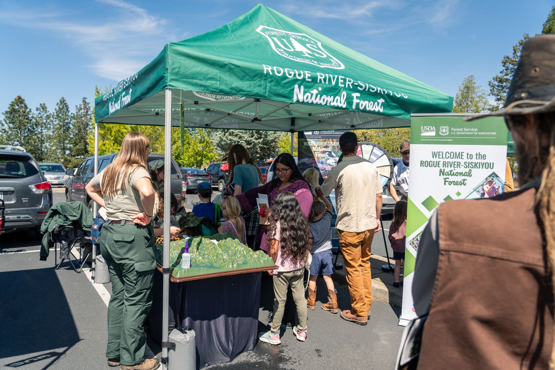 People gathered around a table under a canopy looking at a 3D model of the cascade range at the earth day celebration at scienceworks