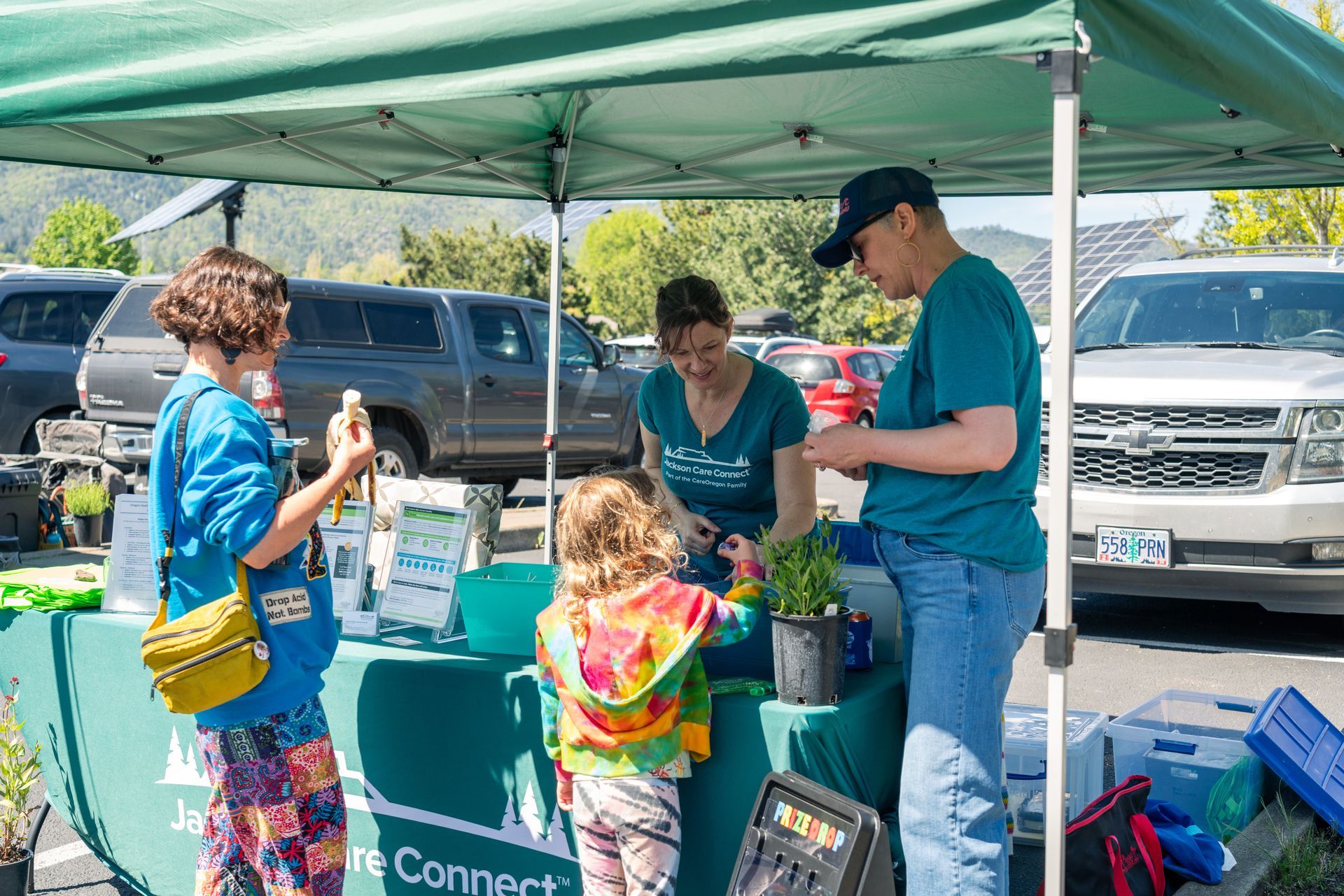 People at an outdoor booth under a green canopy, sharing items on a table and talking.