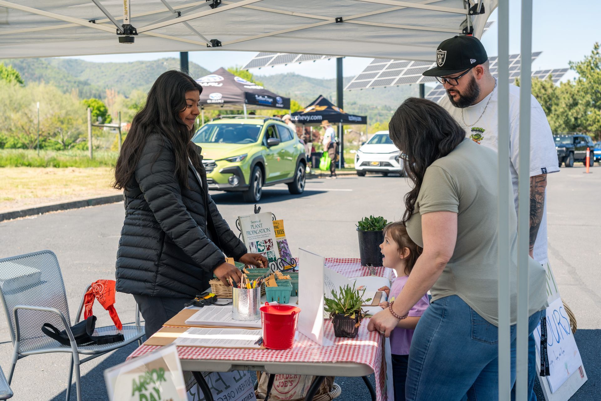 People at a community outreach booth under a white tent, with children gathered around tables of materials.