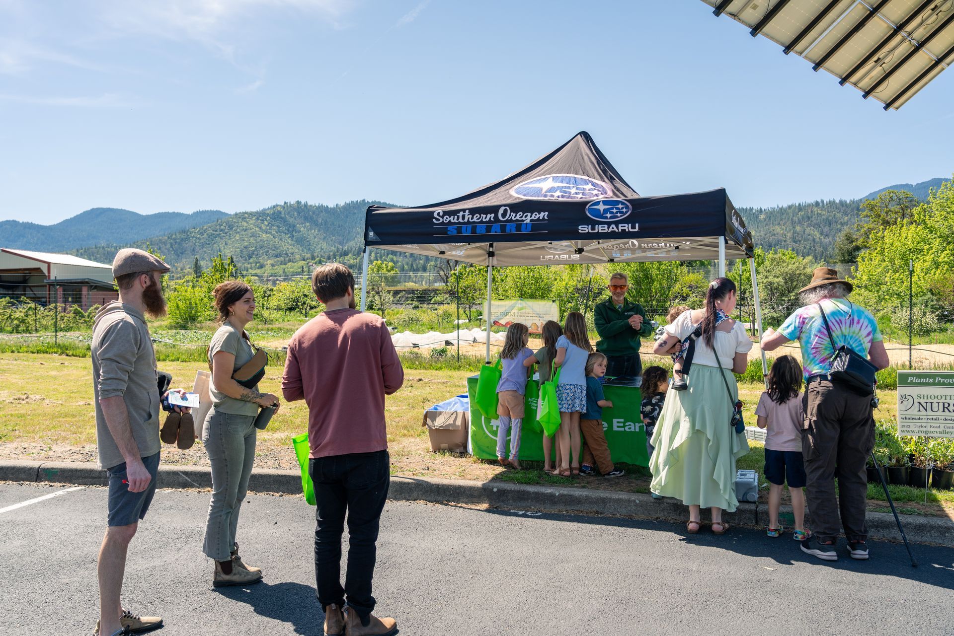 People gathered under a black canopy at an outdoor event with mountains in the background.