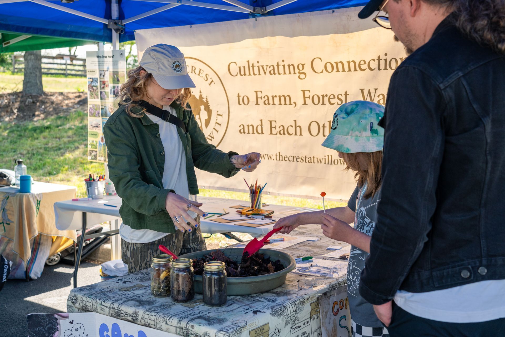A child playing with soil at an event booth under a blue canopy