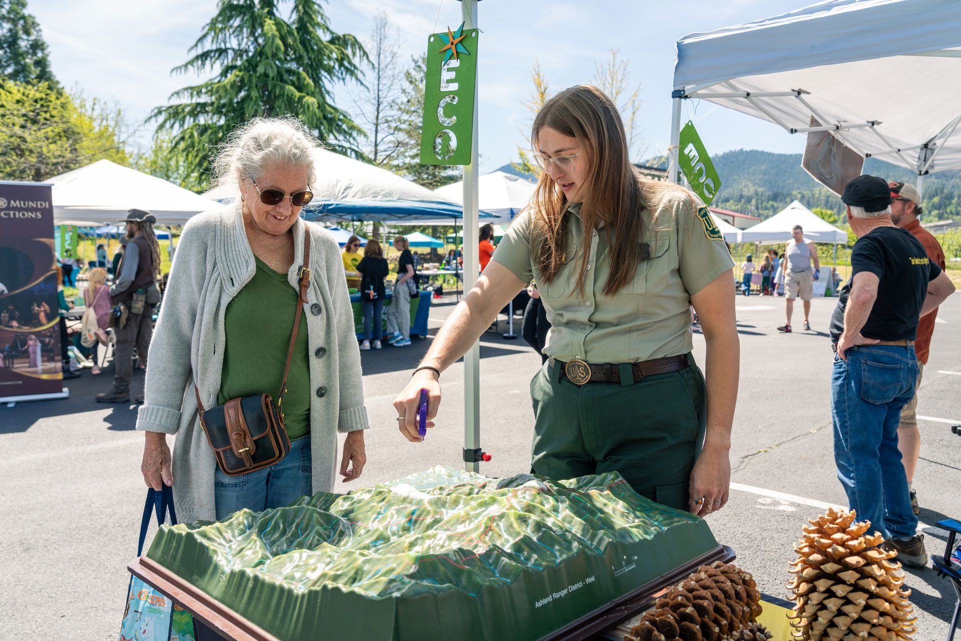 Two people examining a topographic display at an outdoor event booth under white tents