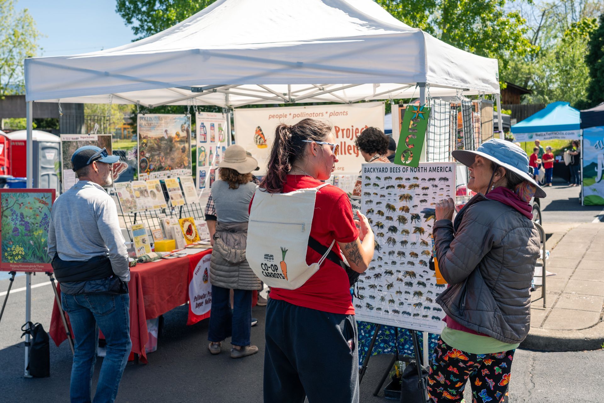 People at a community outreach booth under a white tent, with children gathered around tables of materials.