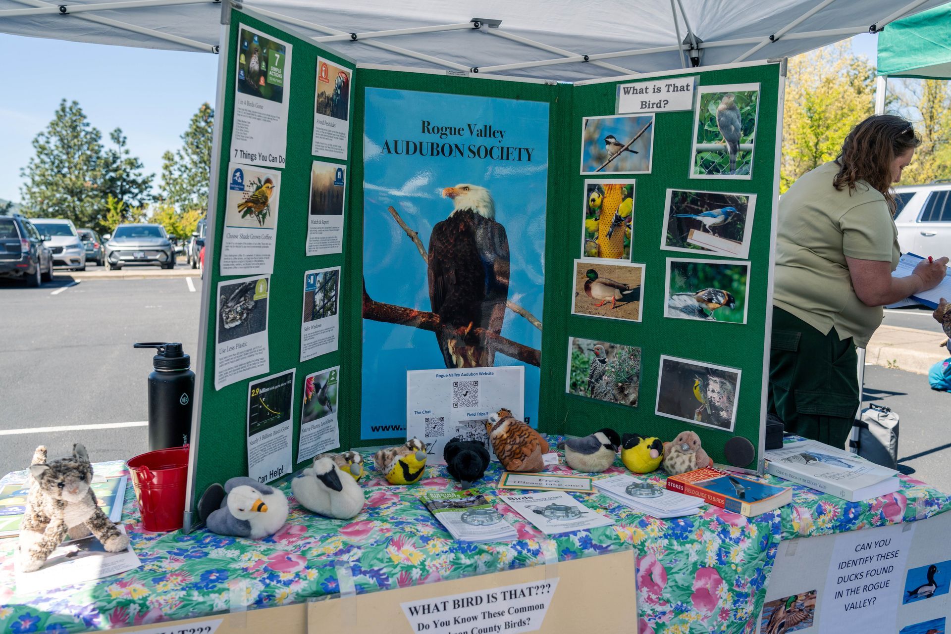 Wildlife rescue booth with bird photos, brochures, and plush animals on a colorful table under a white tent