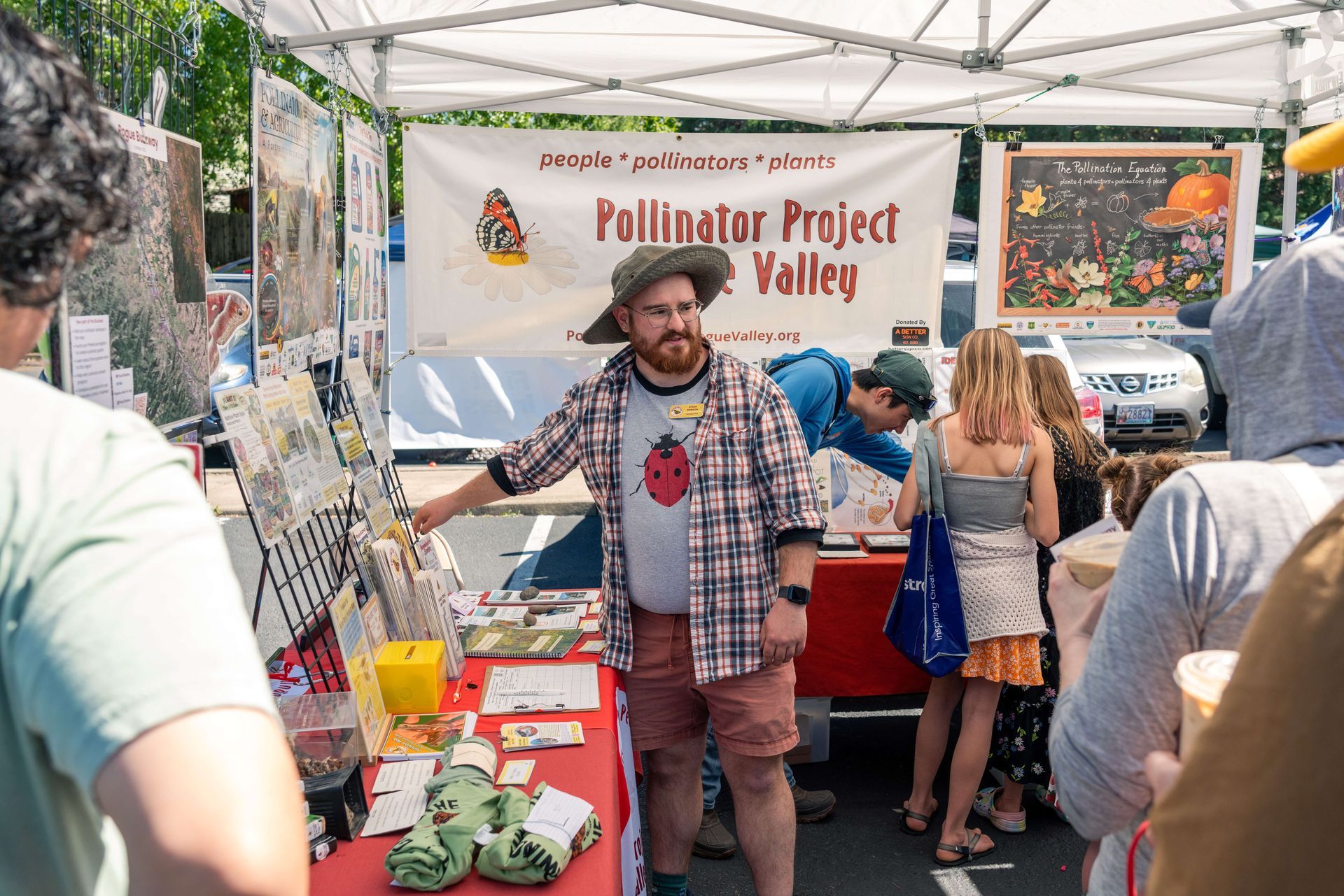 People at a community outreach booth under a white tent, with children gathered around tables of materials.
