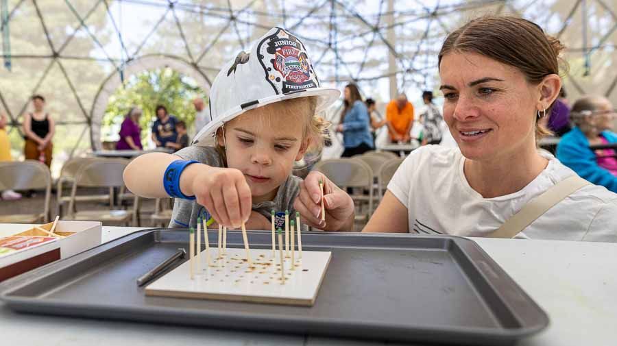 Young child and their mother placing matches in a scientific a tool designed to demonstrate fire behavior at Sparking Action event at ScienceWorks.