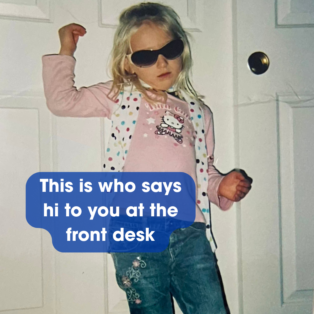 A child with sunglasses stands against a door wearing a pink Hello Kitty shirt and jeans. Text reads: This is who says hi to you at the front desk.