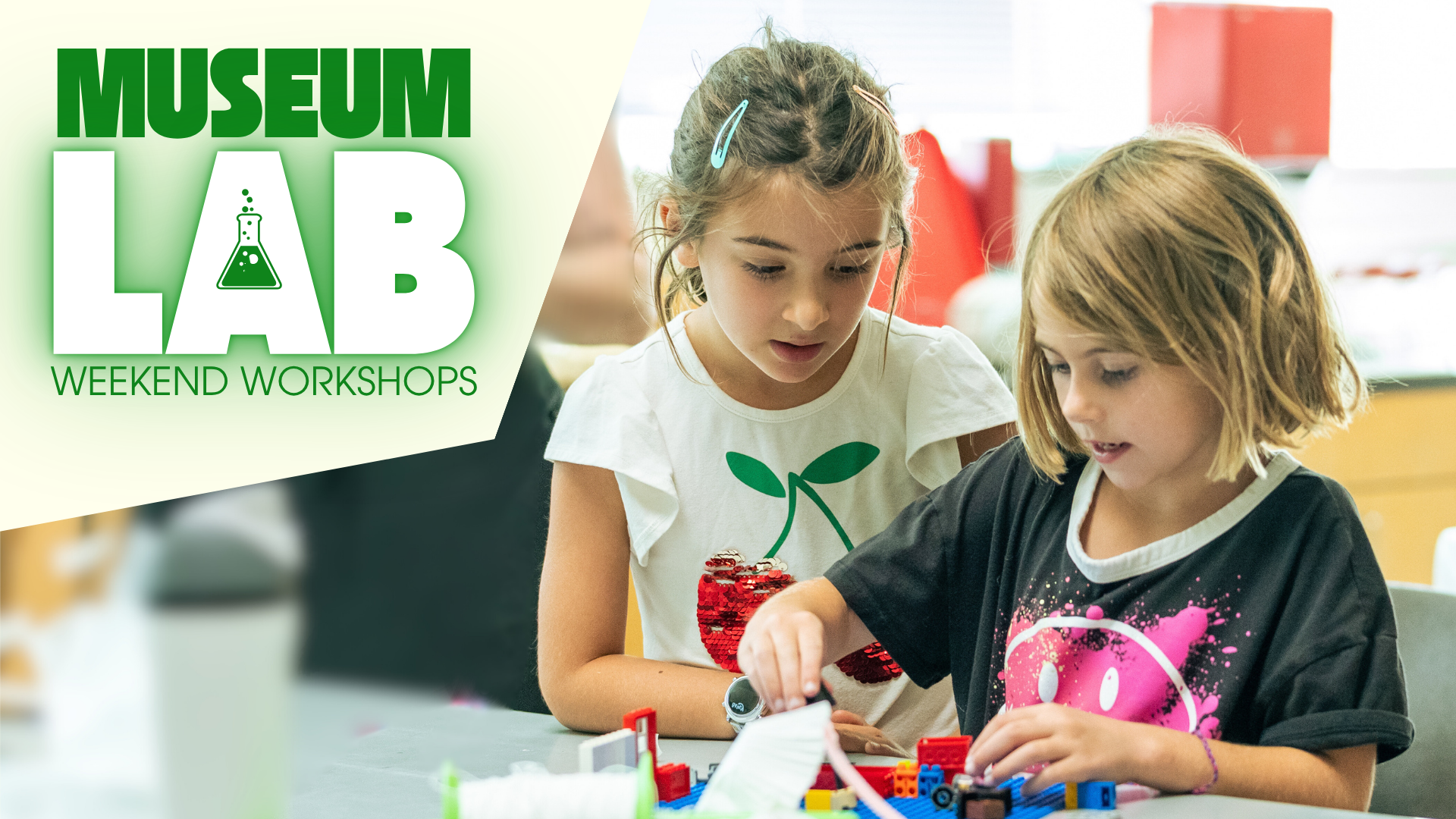 Two children focus intently on building with colorful blocks at a table under a Museum Lab Weekend Workshops logo.