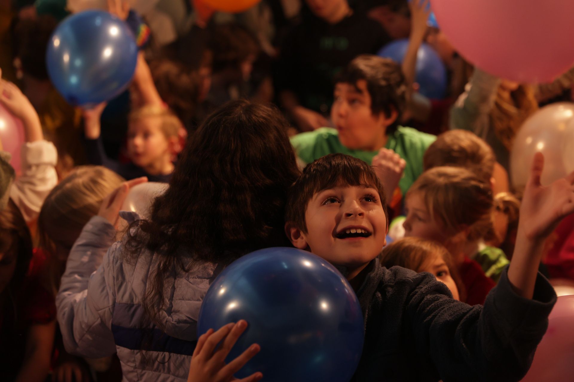 Children with balloons, reaching up excitedly. Group scene, indoor, many balloons at ScienceWorks.