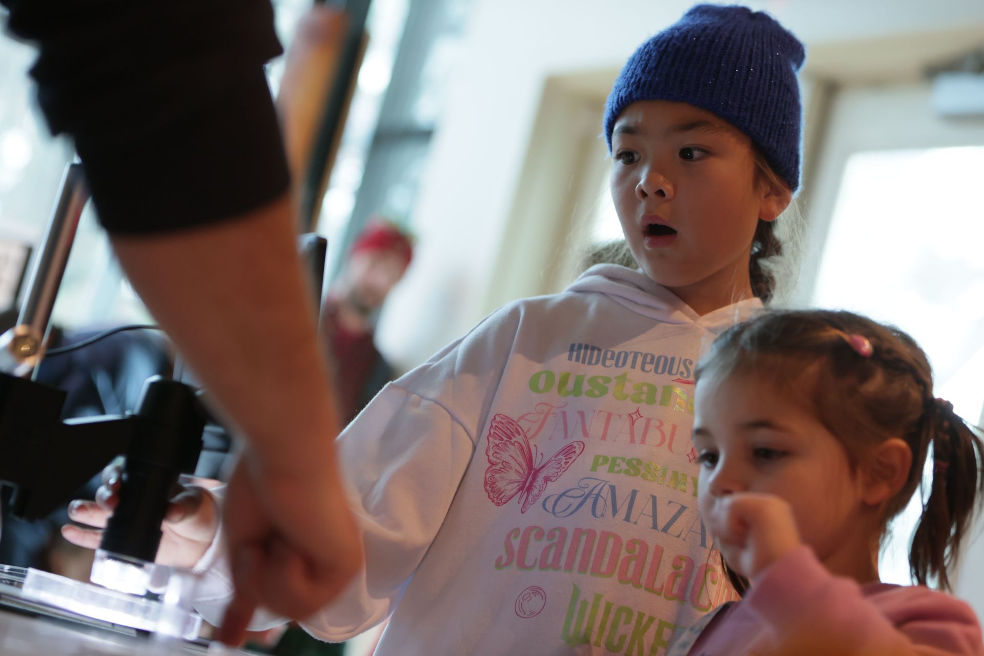 Two girls looking surprised as an adult points to an object in a laboratory setting at ScienceWorks.
