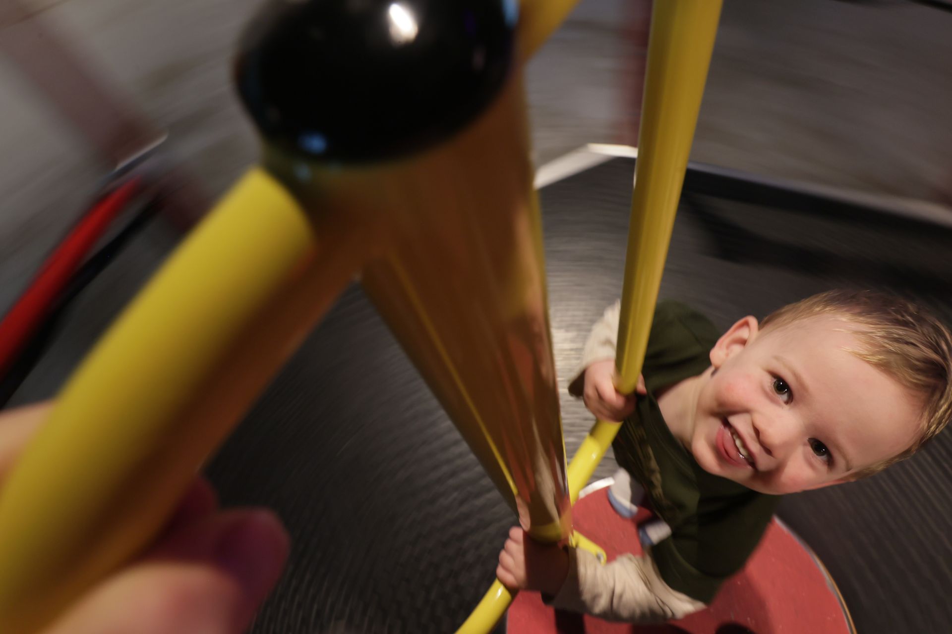 Child smiles while playing on a yellow spinning platform  at ScienceWorks. Indoor setting.