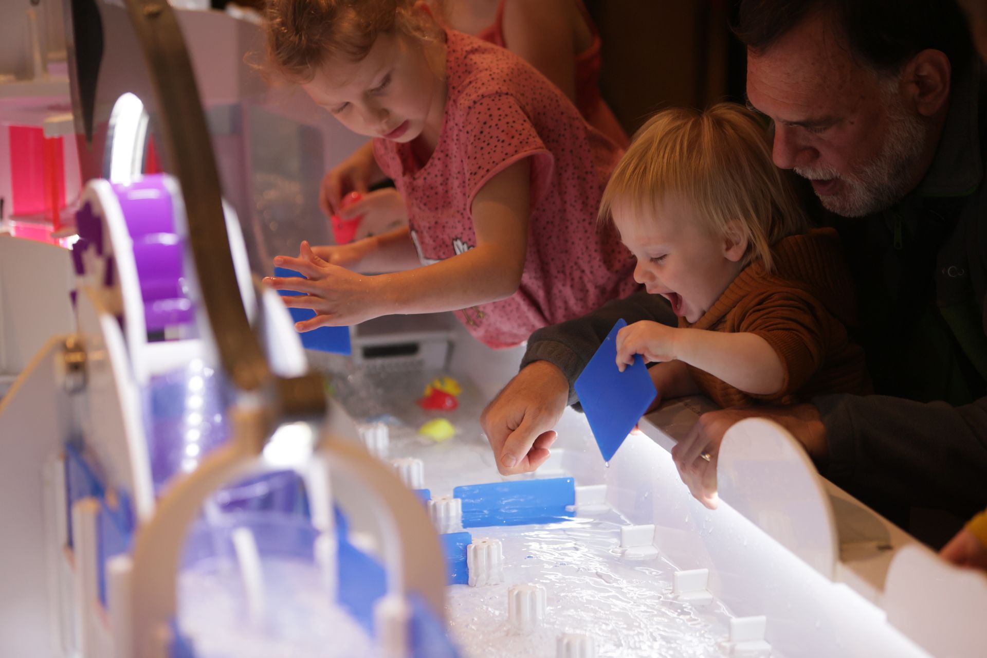 Children and adult playing with water toys in a brightly lit exhibit at ScienceWorks.