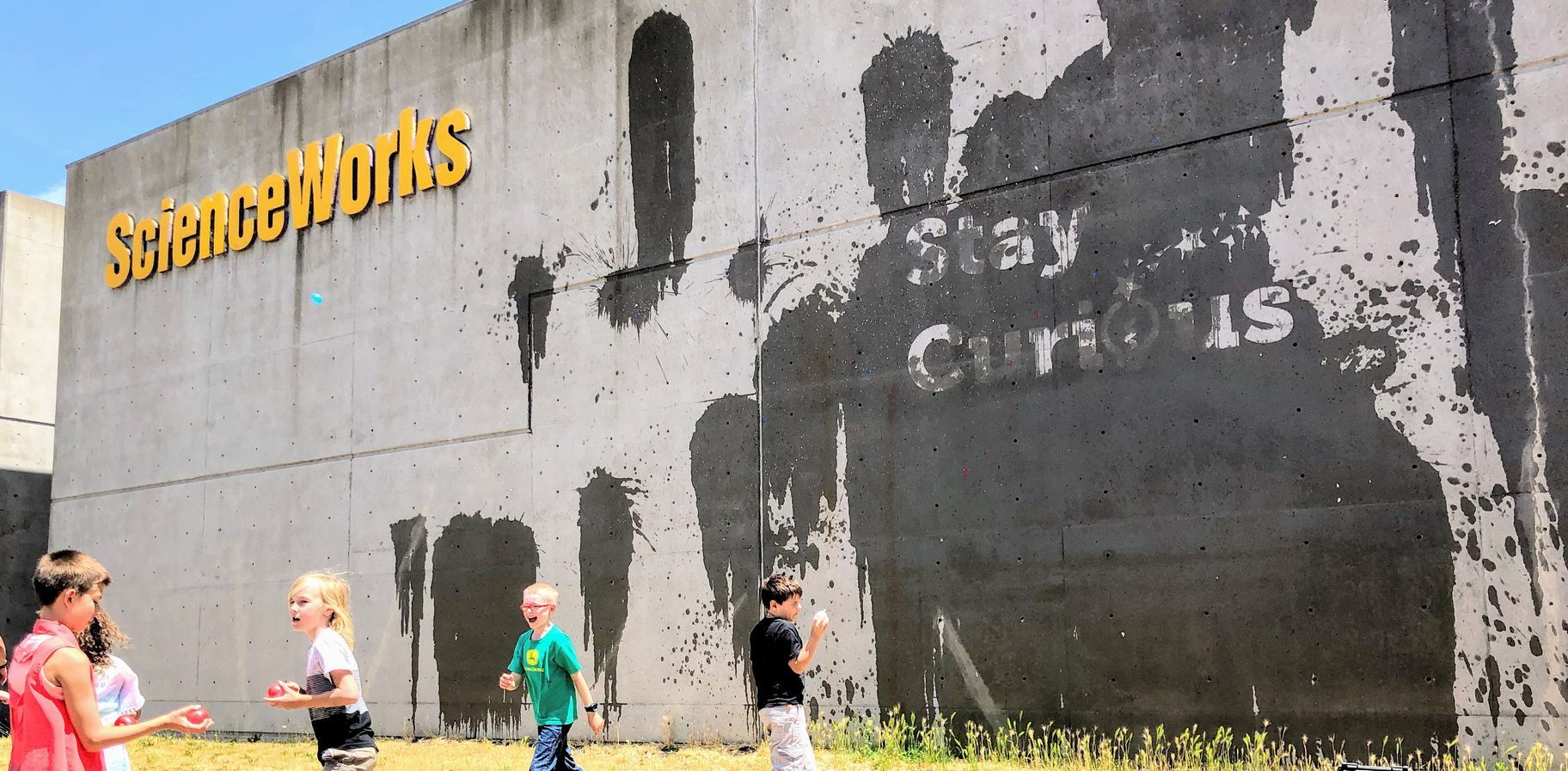 The side of the ScienceWorks building showing young people throwing water balloons at the wall. A sign says 