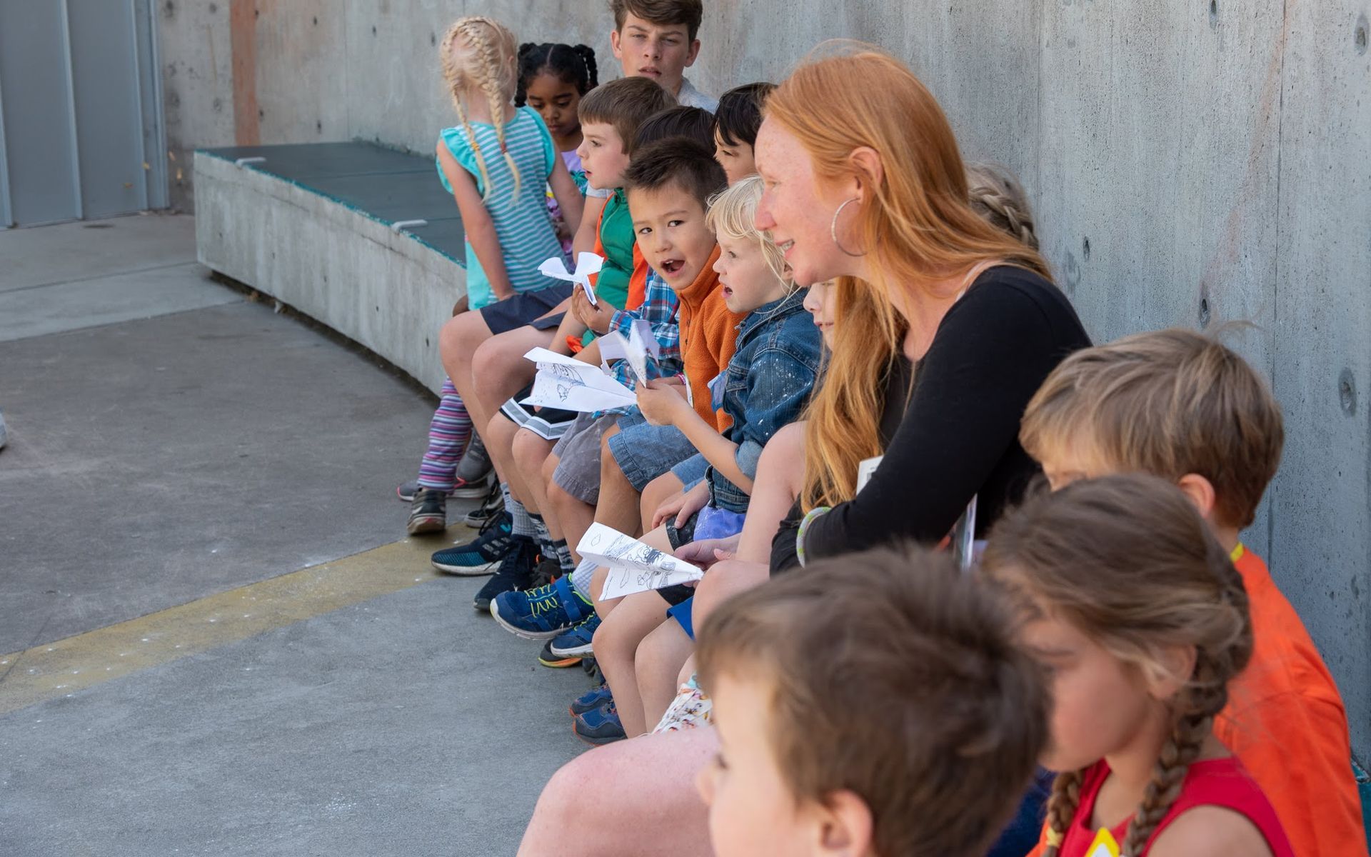 Camp counsellor and group of young campers sit against the wall outside of ScienceWorks