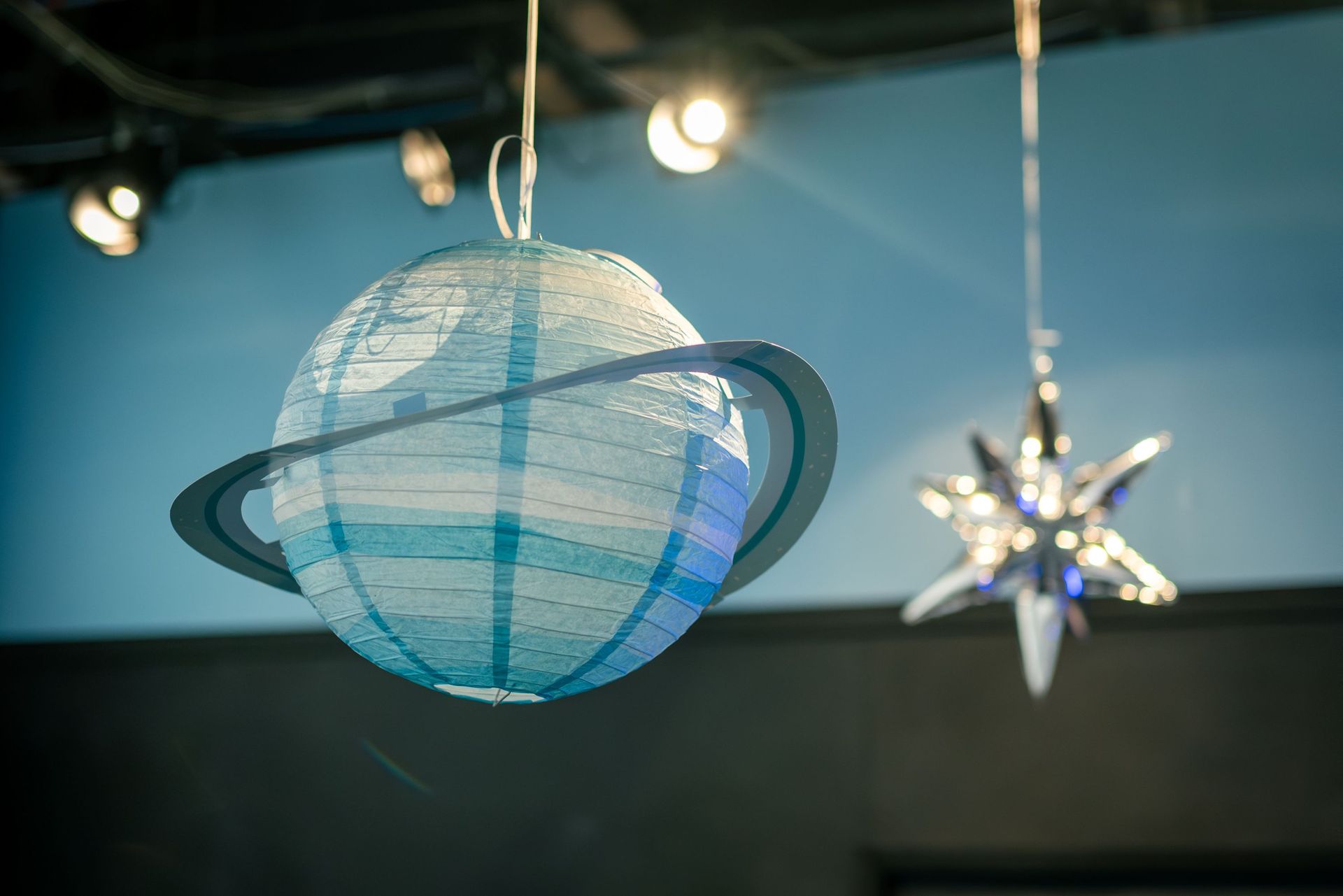 Blue paper planet with rings hanging indoors beside a star ornament under lights