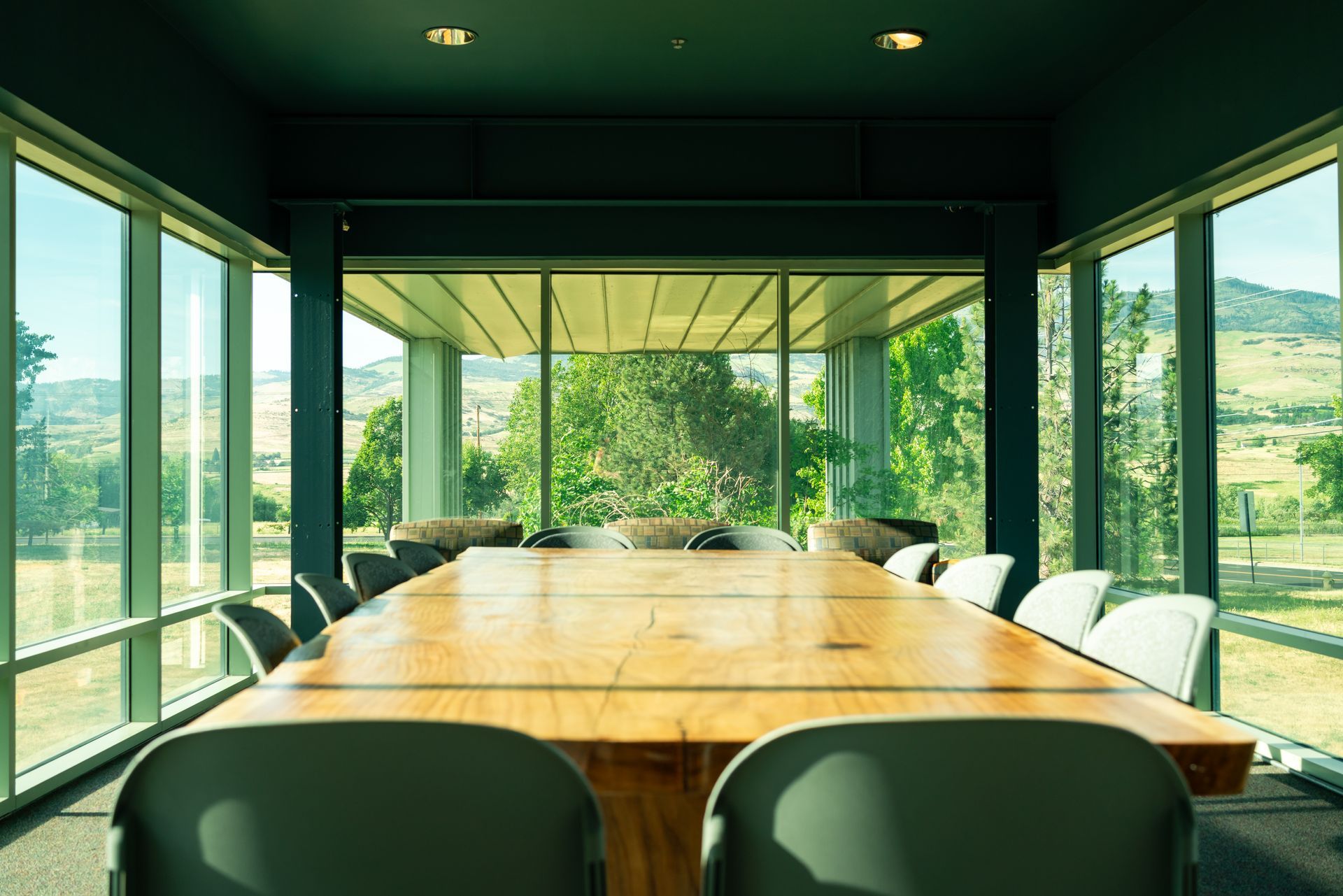 Modern conference room with a long wooden table, green chairs, and large windows overlooking a sunny landscape