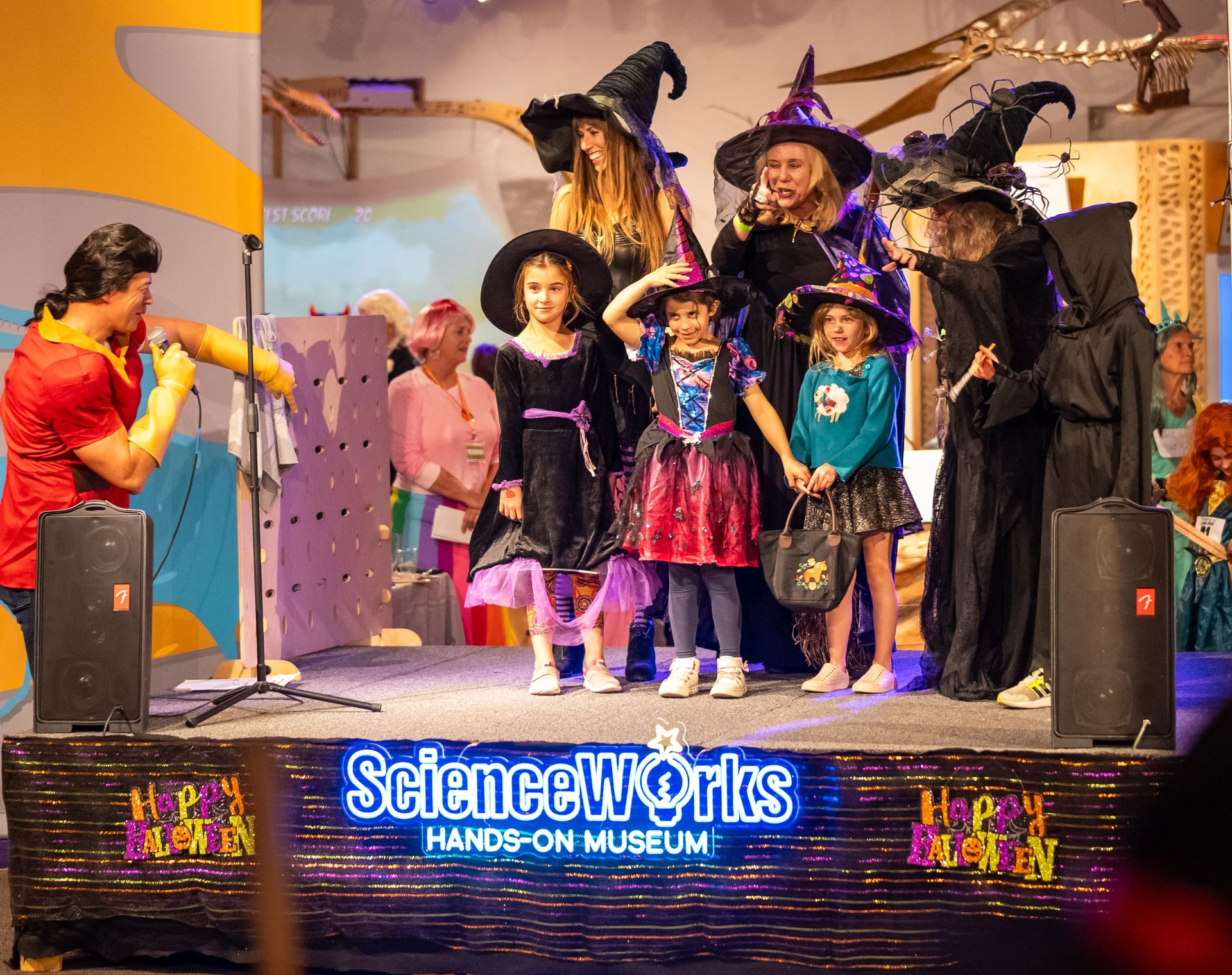 Two children in costumes play with bubbles outside. The boy wears a pumpkin costume, and the girl is dressed as a Queen.
