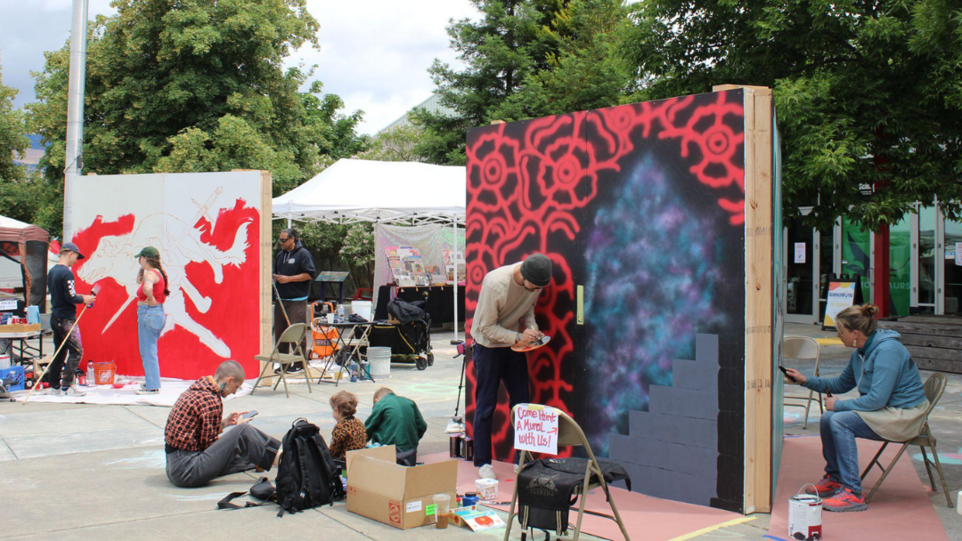 Outdoor mural painters working on large colorful graffiti panels in a public square