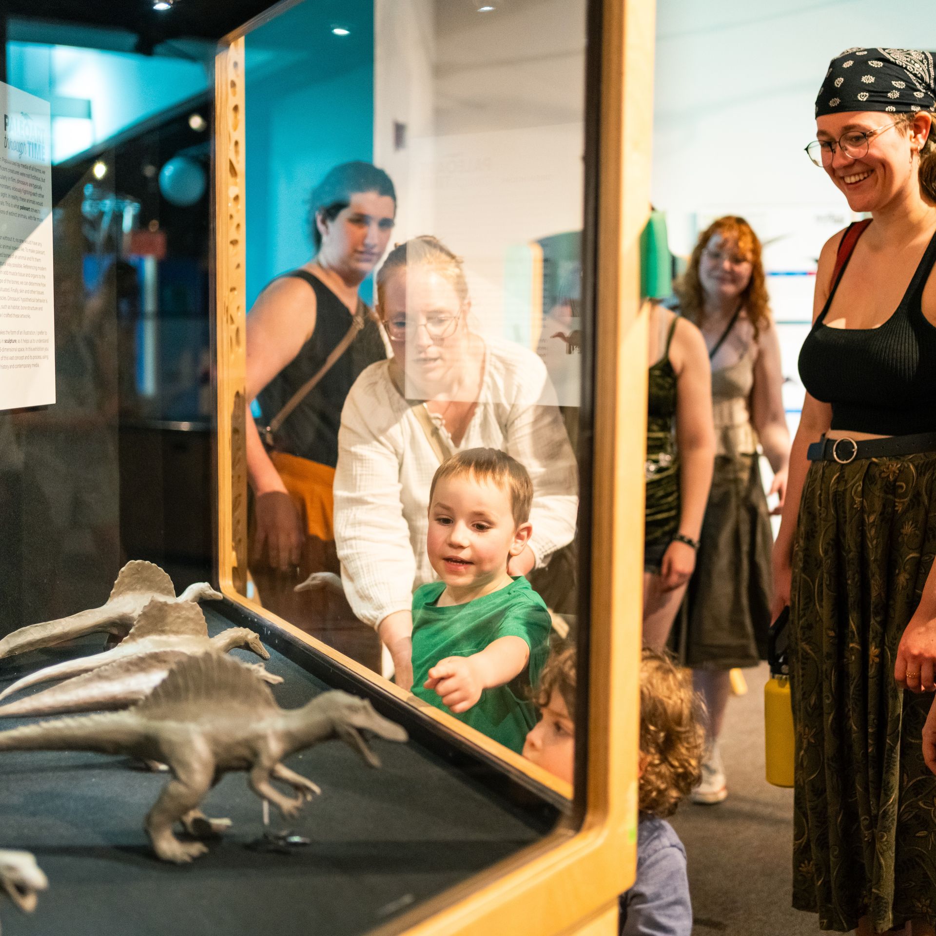 a child and several adults examine replicas of dinosaurs at the paleoart exhibit at ScienceWorks