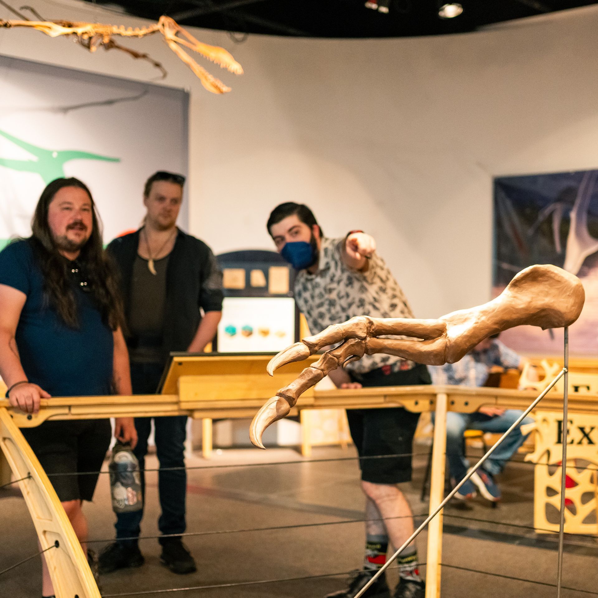 three adults examine a replica of a t-rex arm at the paleoart exhibit at ScienceWorks