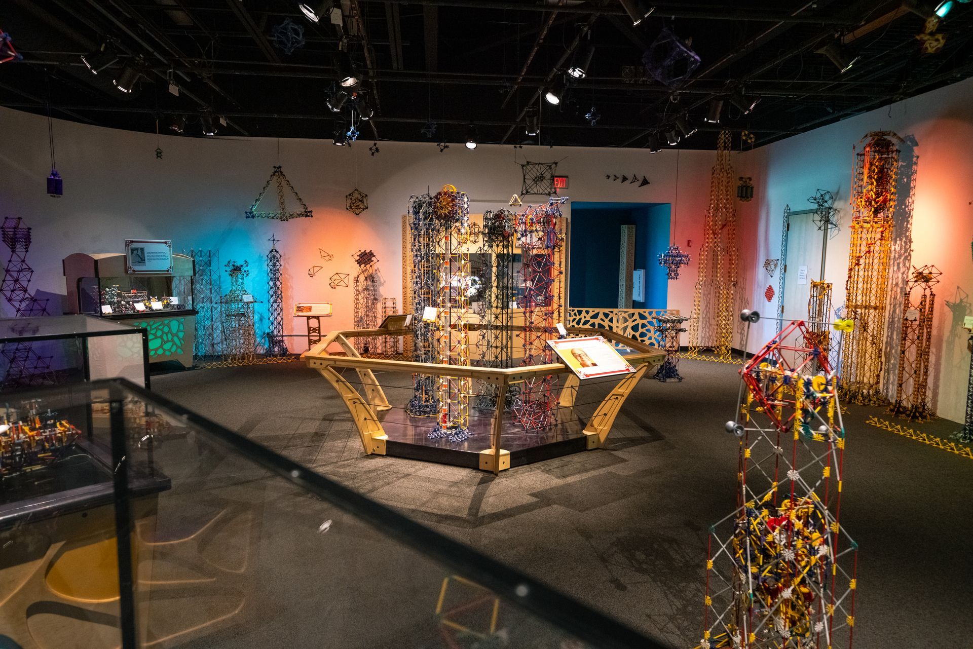 Exhibit hall with colorful hanging sculptures and a central abstract installation under gallery lighting