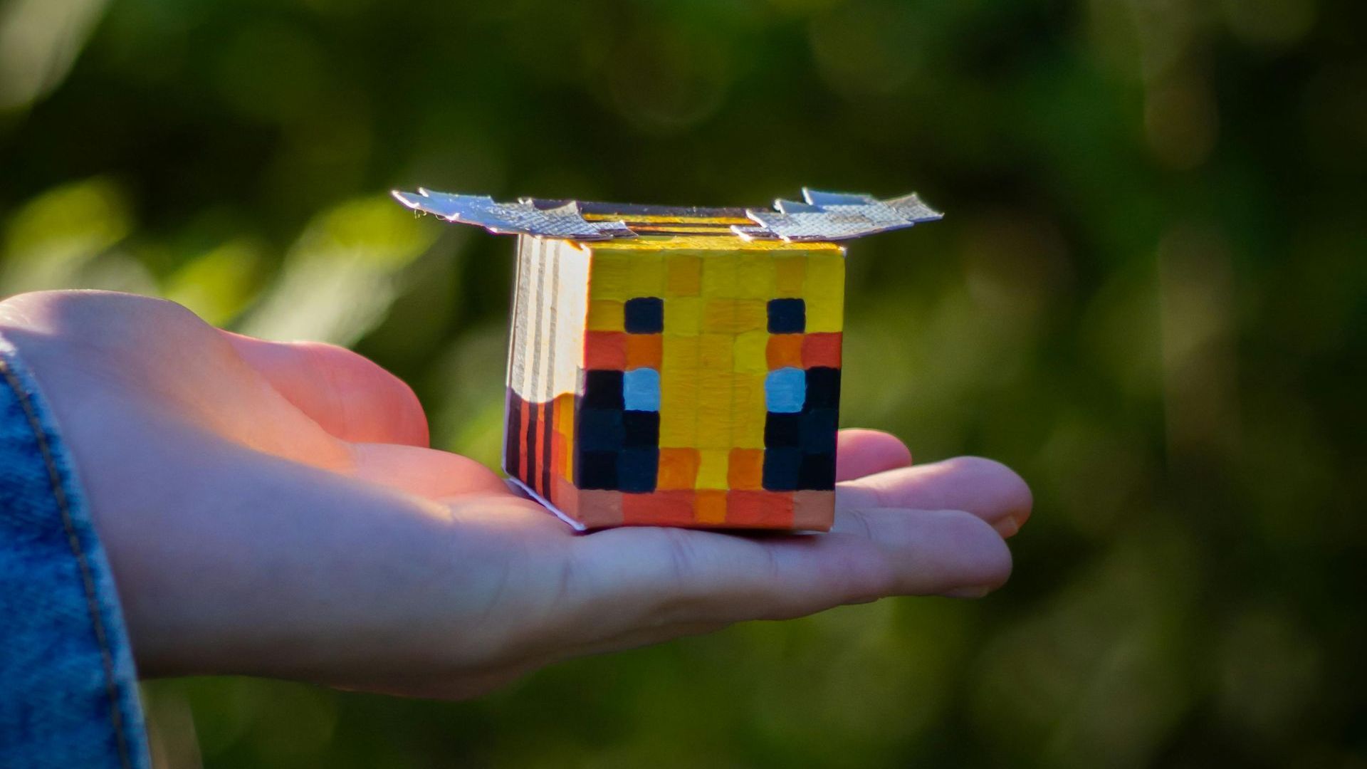 A minecraft bee made of paper held up by a hand