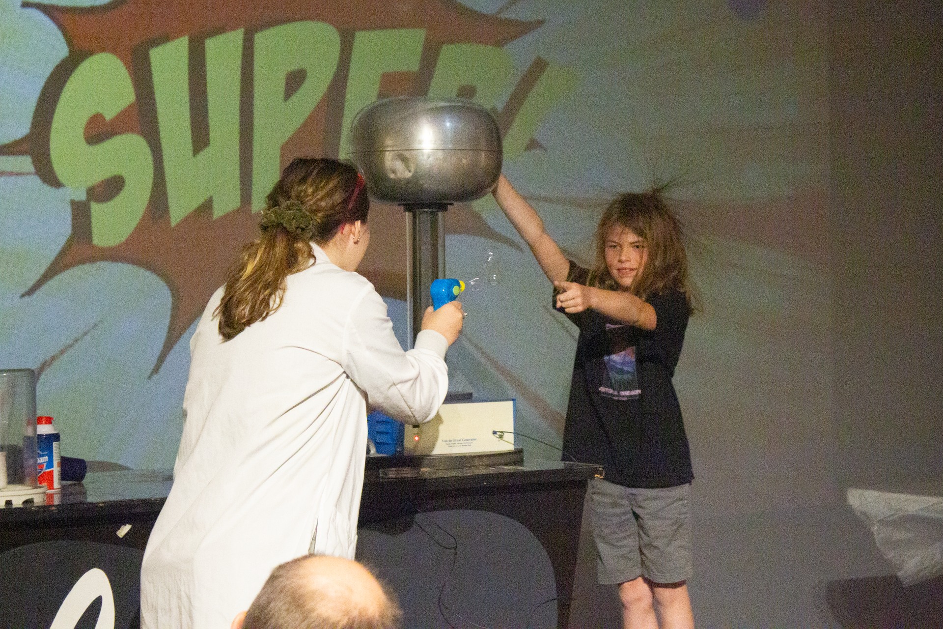 An educator facilitating a superheroes-themed Science Live show for a group, and a student is participating on stage.