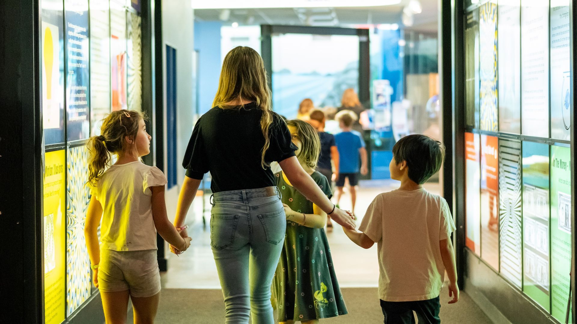 a photo of a teen girl leading a group of younger campers through the hall of illusions at ScienceWo