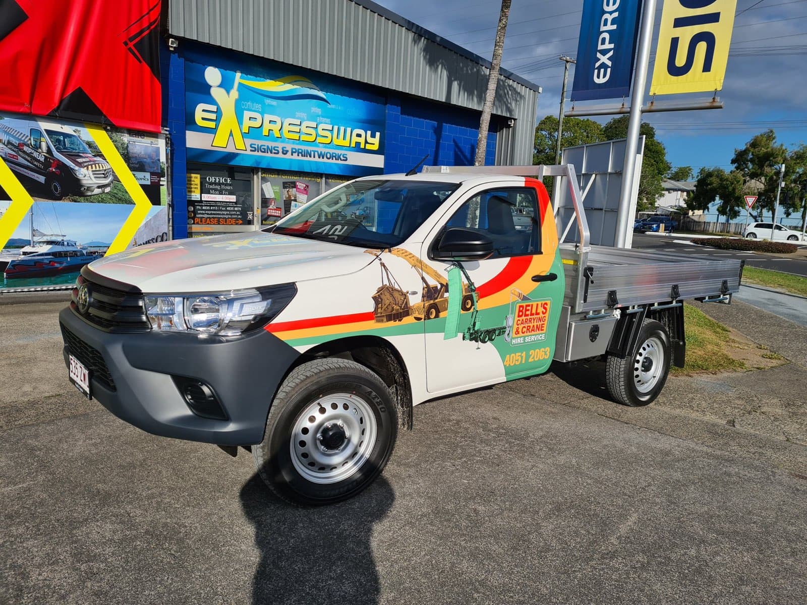 A White Truck With a Flat Bed is Parked in Front of a Building — Bell's Carrying & Crane Hire Service Pty Ltd in Bungalow, QLD