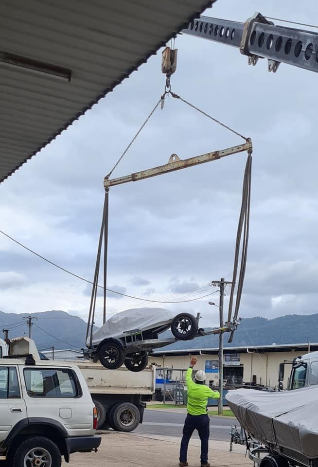 A Man is Lifting a Boat Trailer With a Crane — Bell's Carrying & Crane Hire Service Pty Ltd in Bungalow, QLD