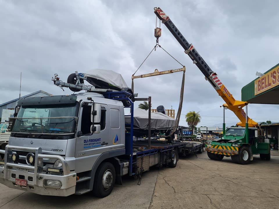 A Truck With a Crane Attached to It is Carrying a Boat — Bell's Carrying & Crane Hire Service Pty Ltd in Atherton, QLD