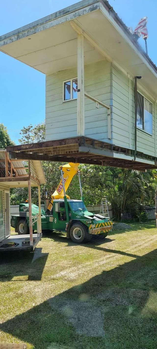 A Green Truck is Carrying a House on a Lift — Bell's Carrying & Crane Hire Service Pty Ltd in Bungalow, QLD
