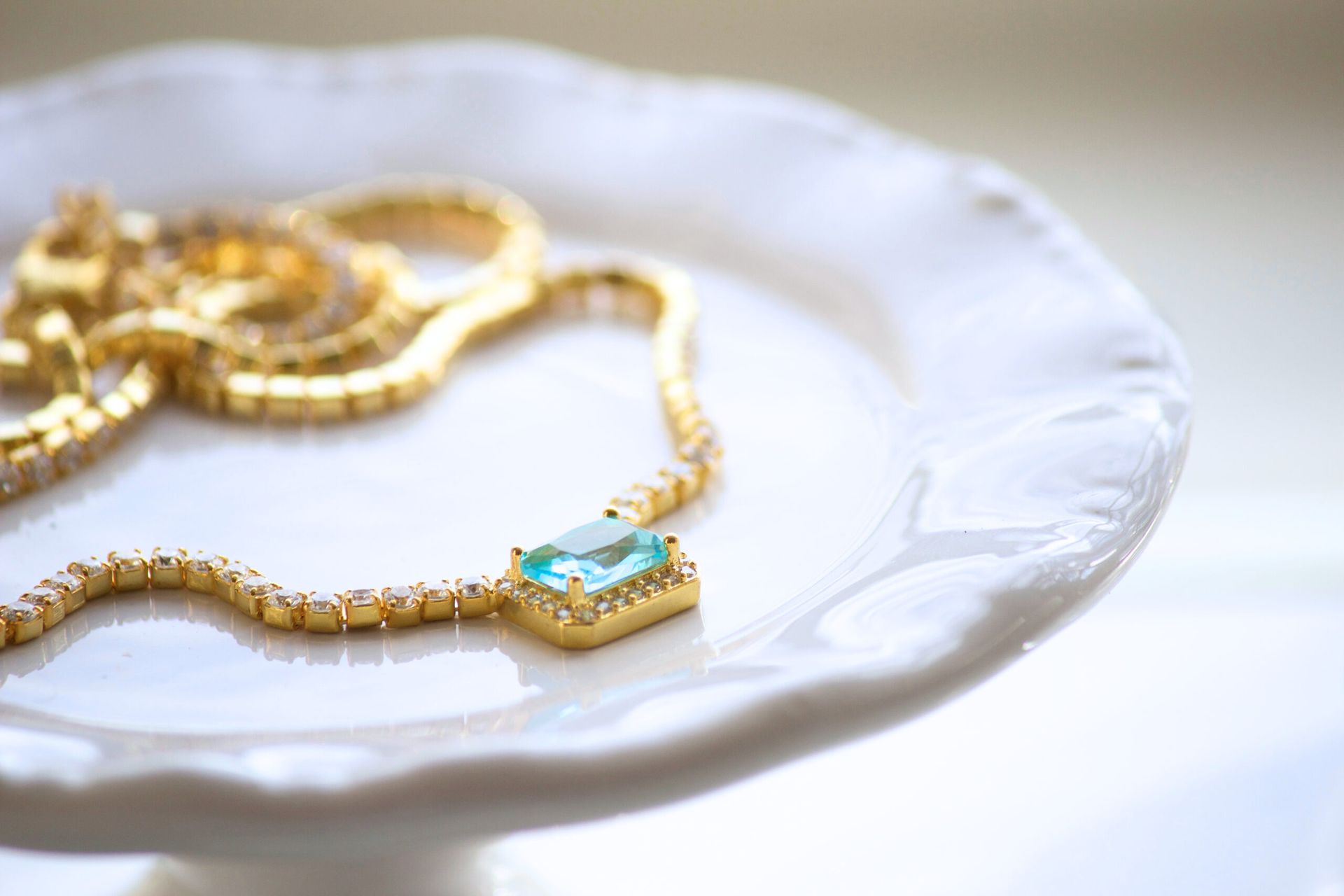 Gold necklace with a turquoise pendant on a white scalloped plate.