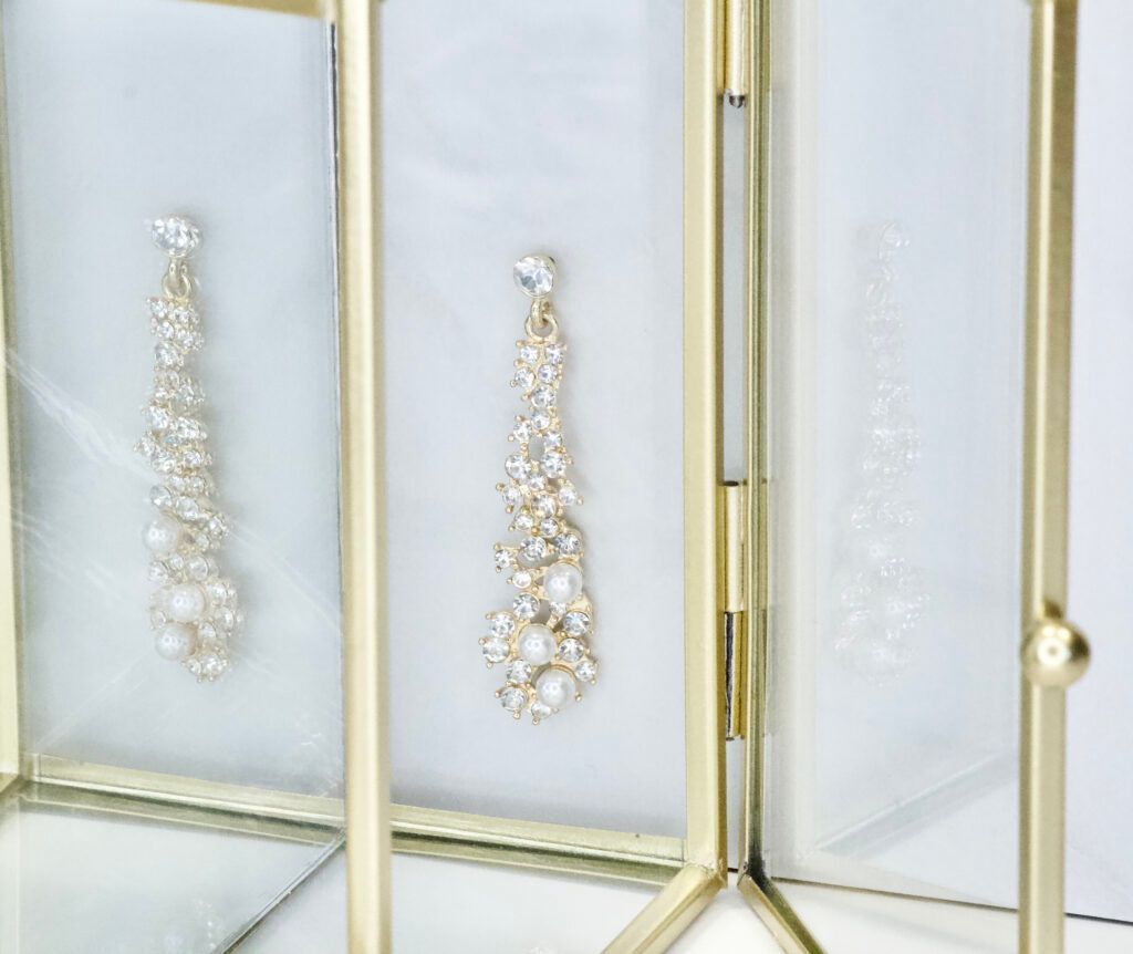 Gold framed display with dangling earrings, showcasing pearls and crystals on a white backdrop.